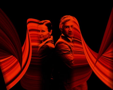 A man and a woman stand back to back with arms crossed. A red light swirls around them.